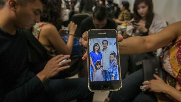A relative showing a picture of alleged passengers who were travelling on missing Malaysian air carrier AirAsia flight QZ8501 on her mobile phone screen at the airport in Surabaya, East Java, on Dec 28, 2014. -- PHOTO: REUTERS
