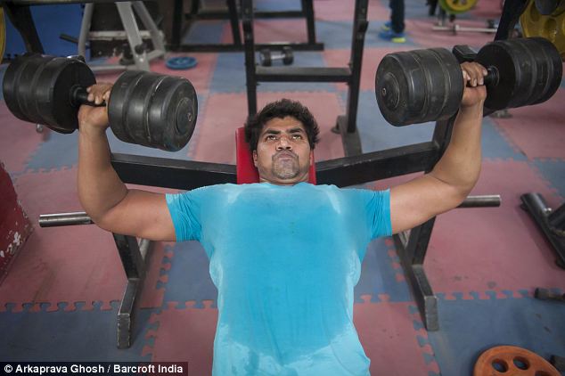 Sweat suffuses the T-shirt of this bouncer as be lifts two heavy weights for a dumbbell bench press