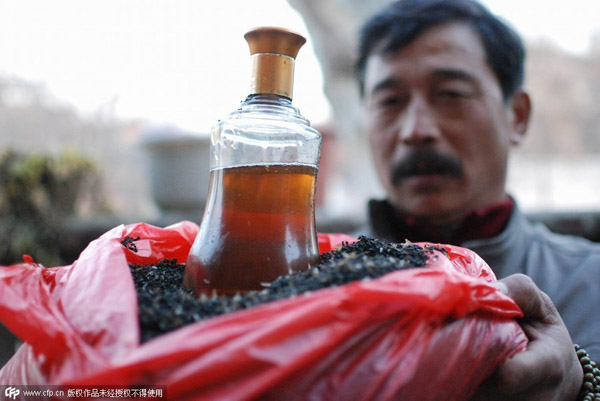 Chen shows fried ants and a bottle of medicinal liquor soaked with silky ants at his home in his village