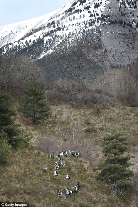 French military personnel walk up the mountainside towards the crash site