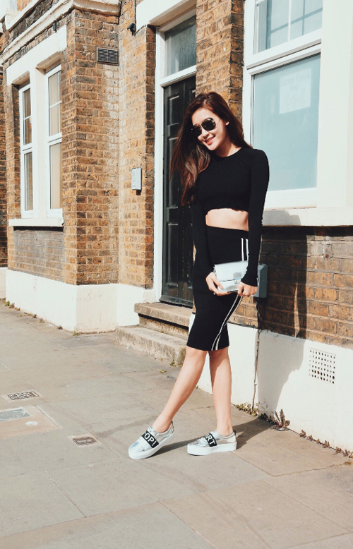 Huyền My v&iacute; cầm tay, gi&agrave;y slip on tr&ecirc;n chất liệu &aacute;nh kim khi sử dụng một c&acirc;y đen.