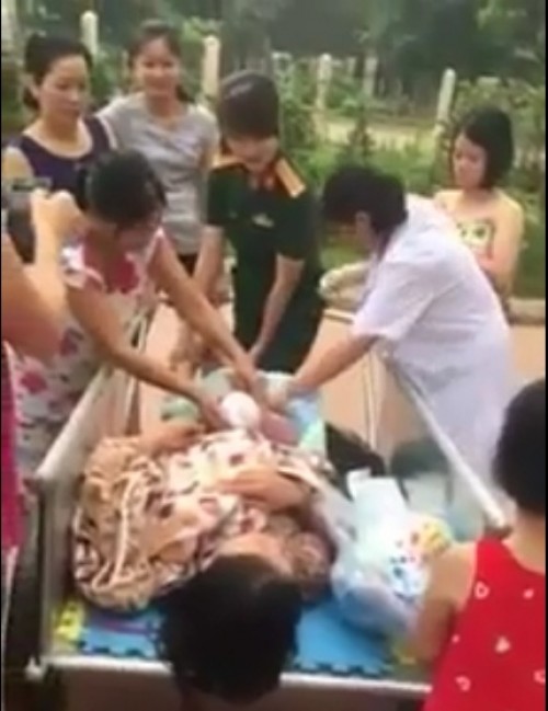 Người dân và cán bộ y tế đỡ đẻ cho sản phụ sinh tại sân chung cư. (Ảnh cắt từ clip)