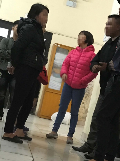 
Bố mẹ C. (hai người mặc áo đen) đứng bên ngoài phòng cấp cứu, nét mặt lo lắng.
