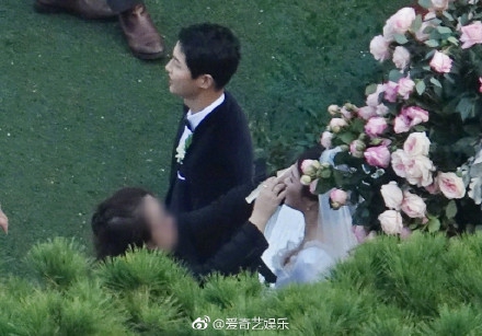 Song Joong Ki đứng cạnh vợ trong lúc cô được trang điểm lại. Nữ diễn viên Song Hye Kyo mặc váy cưới trắng cúp ngực.