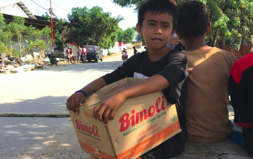 Mohammed Idhan, 12 tuổi, cầm hộp các-tông đứng xin tiền bên đường cho gia đình. Ảnh: Telegraph