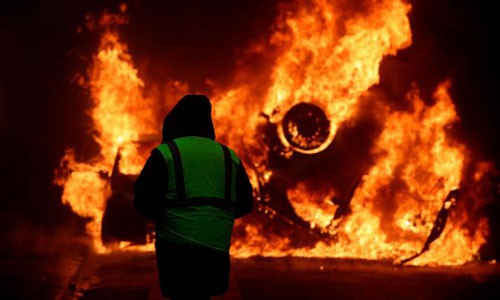 Một người biểu tình mặc áo vàng nhìn chiếc ôtô bị đốt cháy gần đại lộ Champs-Elysees hôm 1/12. Ảnh: CNN.