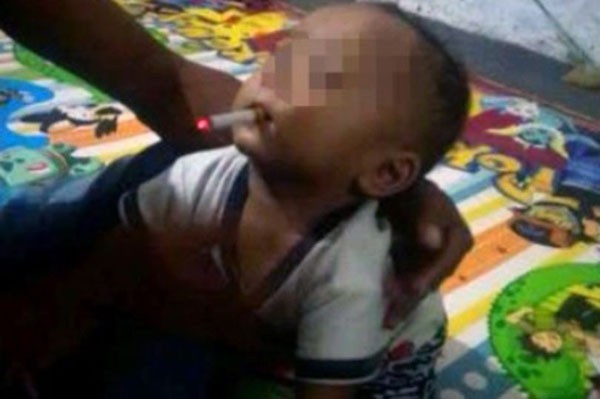 Ông bố trẻ đỡ con trai 9 tháng tuổi khi cậu bé ngậm điếu thuốc cháy dở trong miệng. Ảnh: AsiaWire