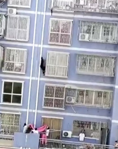 Cư d&acirc;n trong t&ograve;a nh&agrave; căng bạt ở tầng 1 đề ph&ograve;ng Zhang ng&atilde; khi tay kh&ocirc;ng tr&egrave;o l&ecirc;n tầng 5. Ảnh: Pear Video.