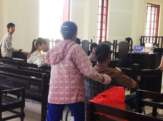 Bà Q. đẩy xe lăn đưa chồng vào vị trí bục khai báo dành cho bị cáo. Ông Nguyễn Thanh An - chồng bà bị truy tố xét xử về tội Dâm ô đối với trẻ em