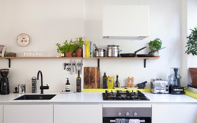 Tiếp nối với khu vực ăn uống là không gian nấu nướng. Chỉ khéo léo tiếp nối với khu vực ăn uống bằng chính gam màu trắng đơn giản và tinh khôi, căn bếp cũng đẹp một cách tự nhiên và bình dị. Hệ thống tủ bếp được lắp đặt phía dưới sàn. Phía trên tường gần với trần được thiết kế kệ gỗ đơn giản để lưu trữ đồ đạc, đồng thời tăng thêm nhiều diện tích đặt cây cảnh tạo nên góc nhỏ vô cùng xinh yêu.