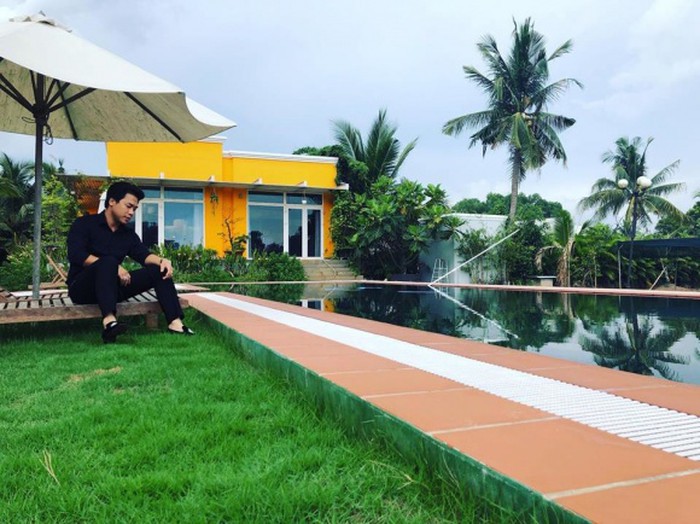 Căn biệt thự được sơn vàng cam nổi bật giữa khu đất đầy cây cối. Một góc biệt thự có hồ bơi xanh mát, sân còn được trải thảm cỏ và có ghế ngồi để nghỉ ngơi, thư giãn.