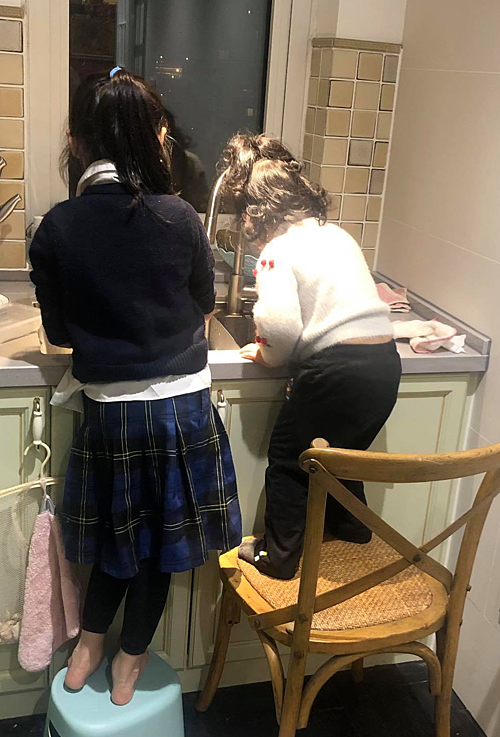 Hai chị em được mẹ chuẩn bị cho ghế để đứng lên khi rửa rau, bát.