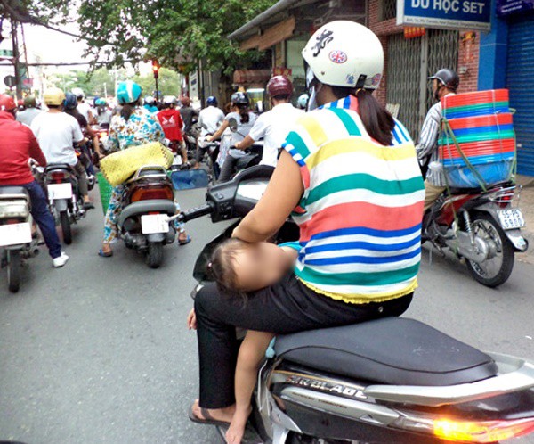 
Đứa trẻ ngủ ngon lành trong lòng và gác đầu lên đùi người mẹ trong khi đó người điều khiển xe máy vẫn vô tư đi xe (ảnh F.B).
