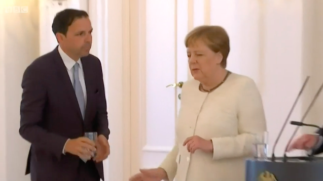 
Một người mang cho bà Merkel cốc nước nhưng bà từ chối. Ảnh: Cắt từ clip BBC
