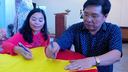 
Tác giả Quế Mai và nhạc sĩ Đinh Trung Cẩn cùng ký tên lên lá cờ Tổ quốc trong buổi ra mắt tập thơ “Tổ quốc gọi tên mình”
