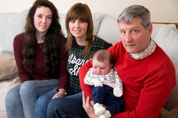 
Ông Rooney bế đứa con được sinh ra từ tinh trùng của mình với trứng một trong hai người của cặp vợ chồng đồng tính.
