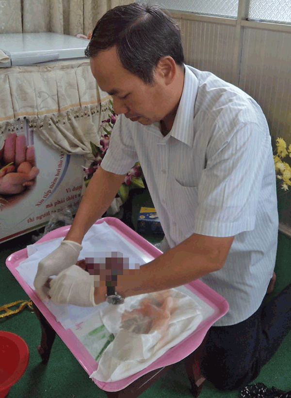
Linh mục Nguyễn Văn Tịch đang liệm cho thi thể c&aacute;c h&agrave;i nhi xấu số
