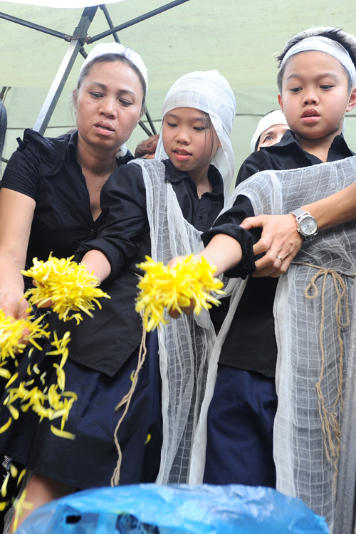 Hai bé Minh Tú (giữa) và Bình Minh cùng họ hàng rải hoa, cầu nguyện cho bố.