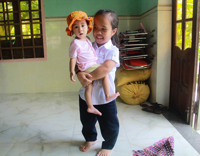 Ngoài giờ đến trường, cô gái phụ giúp cha mẹ trông em. Ảnh: Nam Cường.