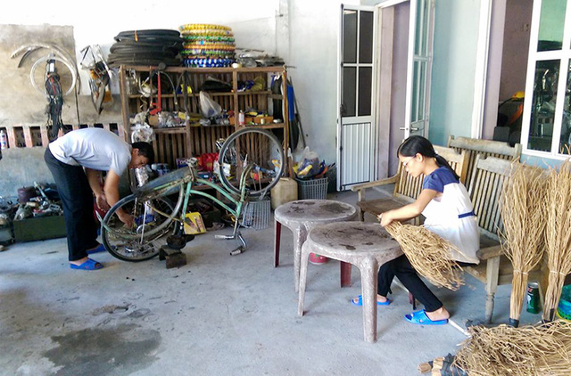 Thầy Sơn sửa xe đạp trong khi vợ thầy bó chổi kiếm thêm thu nhập.