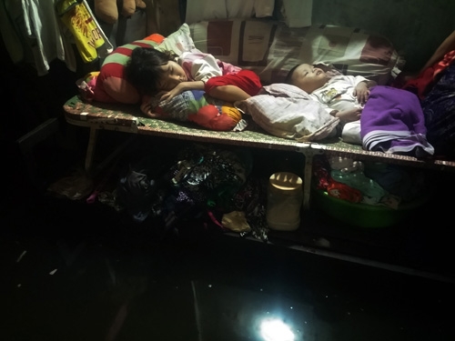 Bé gái 7 tuổi cùng em trai 6 tháng tuổi đang say giấc trên chiếc giường xếp trong phòng trọ ngập nước.