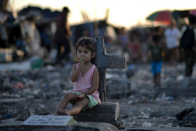 
Một bé gái ngồi cạnh tấm bia mộ giữa một khu ổ chuột bên trong nghĩa địa ở thị trấn phố Navotas, thuộc thủ đô Philippines, ngày 29/10/2015.
