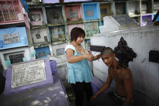 
Người phụ nữ cắt tóc cho một người đàn ông trước một ngôi mộ trong nghĩa trang Bắc Manila ngày 28/10/2011.
