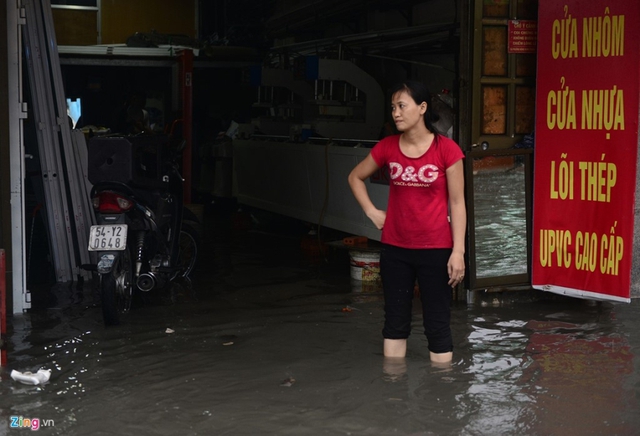 Chị Đào Thị Oanh đứng nhìn biển nước khi cửa hàng bán cửa nhôm, nhựa bị ngập. Trước đây mưa lớn chỉ ngập nhẹ rồi rút, từ khi công trình chống ngập xây dựng thì ngập càng nặng hơn, người phụ nữ này cho hay.