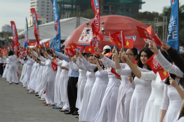 Trên bờ các nam sinh, nữ sinh xinh đẹp đứng vẫy cờ chào đón đoàn...