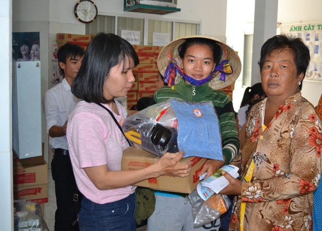 Một phụ nữ chân tay yếu do bệnh phải nhờ người khác hỗ trợ nhận quà.