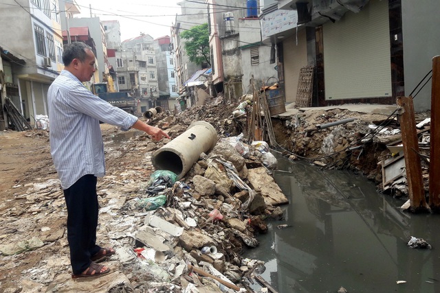 Ông Trần Tam Hảo (67 tuổi) đang chỉ xuống dòng nước ô nhiễm của con mương Y Khoa làm phát sinh nguy cơ dịch bệnh do muỗi. Ảnh: C.Tuân