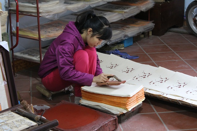 
Cô con gái nhà nghệ nhân Nguyễn Hữu Quả ngồi đóng khuôn tranh lên giấy dó. Khách ít nên gia đình không thuê thêm nhân công. Ảnh: Xuân Hải
