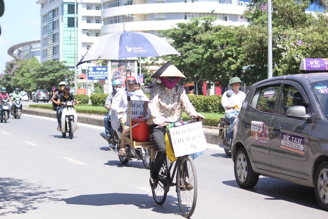 
Một người phụ nữ bán thạch dừa dùng một chiếc ô để che nắng khi đi bán hàng.
