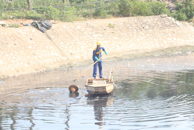 
Một nhân viên môi trường vớt rác thải trên dòng nước đen đặc của sông Tô Lịch
