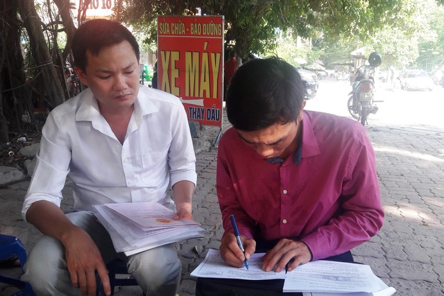 Một đối tượng “cò viết chữ” (bên phải) chuyên chèo kéo viết hồ sơ thay người dân với giá 200.000 đồng tại hành lang Văn phòng đăng ký đất đai Hà Nội.