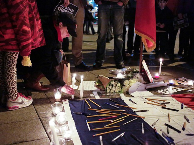 People place pens, pencils and candles around a French flag at a vigil outside the French consulate in Seattle, Washington, Wednesday night for the victims of the shooting at the Paris offices of the publication Charlie Hebdo.