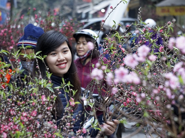 Một cô gái bán hoa đào cùng nụ cười tươi đón khách mua đào sớm.