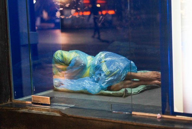 
Một người lao động ngủ co ro trong cây ATM bên đường.
