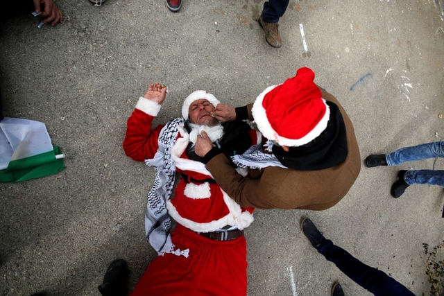 
Một người biểu t&igrave;nh Palestine trong trang phục &ocirc;ng gi&agrave; Noel đang được chăm s&oacute;c sau khi tr&uacute;ng phải hơi cay của qu&acirc;n đội Israel h&ocirc;m 23/12. C&ugrave;ng ng&agrave;y 23/12, Hội đồng Bảo an Li&ecirc;n Hợp Quốc y&ecirc;u cầu Israel ngừng x&acirc;y dựng c&aacute;c khu định cư tr&ecirc;n l&atilde;nh thổ Palestine - Mỹ bỏ phiếu trắng gi&uacute;p nghị quyết được th&ocirc;ng qua. Ảnh: Reuters
