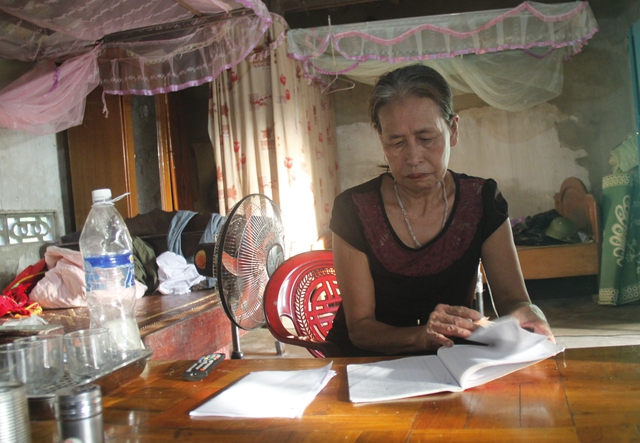 Bà Lâm Thị Lai đang ngồi tìm các giấy tờ để trình bệnh viện miễn giảm tiền ăn, tiền giường cho chồng.