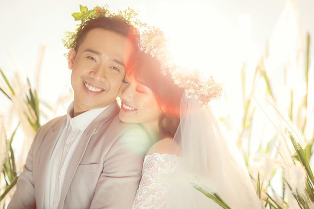 Trấn Thành và Hari Won trong trang phục cưới lãng mạn, với bối cảnh là trên một đồng cỏ lau.