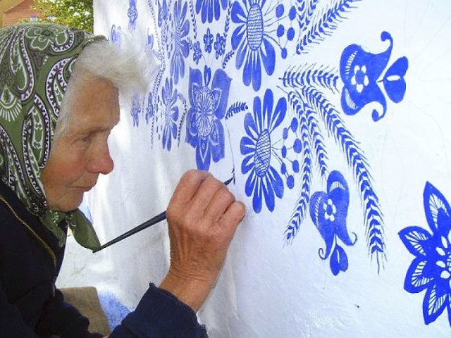 Cụ bà Anežka đang tỉ mẫn vẽ những hoa văn màu xanh dương trên nền tường trắng