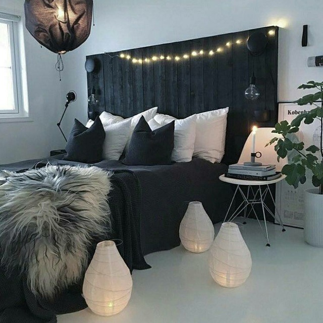 Giường nệm với bảng đầu giường bằng gỗ pallet được sơn màu tối, tô điểm với những chiếc đèn dây và đèn giấy độc đáo.