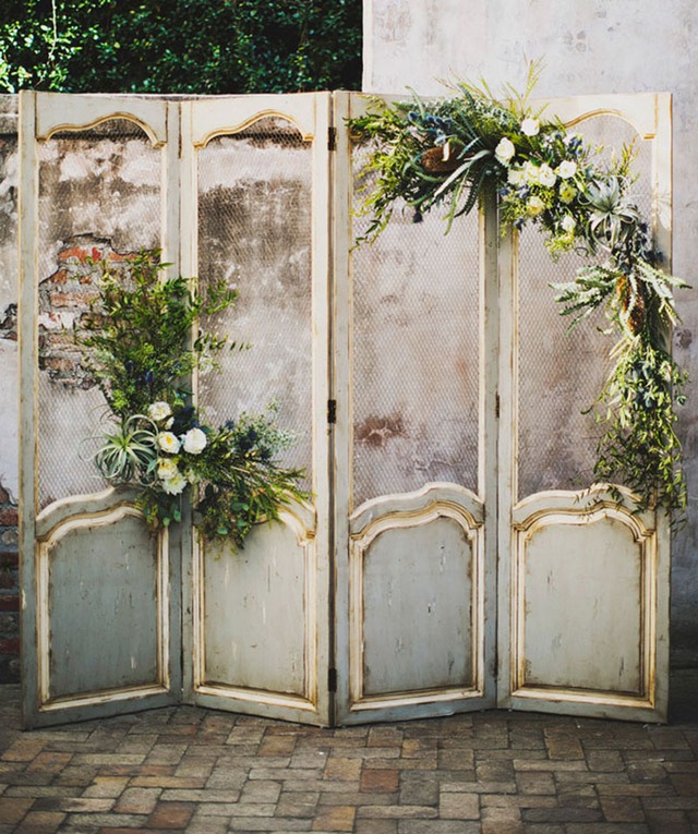Đặt vài cánh cửa gỗ cũ theo phong cách vintage làm một bức tường tiệc cưới. Bổ sung thêm hoa và lá cây để chúng trông mềm mại hơn.