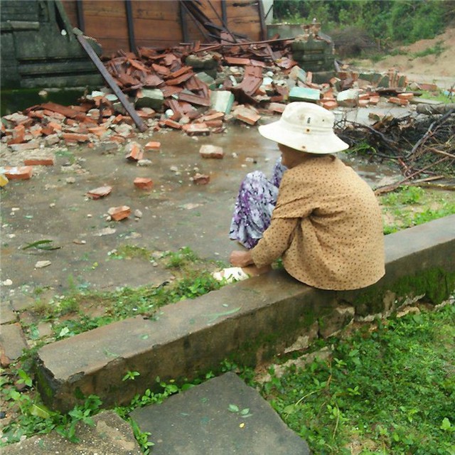 
Bà cụ ngồi trông về phía căn nhà nhỏ đã bị đổ sập. Ảnh: Facebook.
