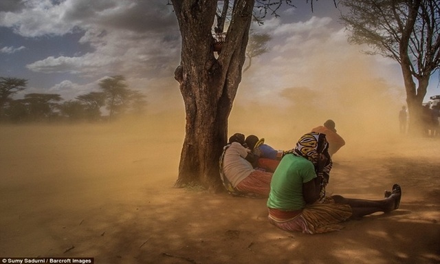 
Những người đàn ông, phụ nữ trong bộ lạc và con cái của họ che cơ thể bằng quần áo truyền thống trong cơn bão cát tại Karamoja, Uganda.

