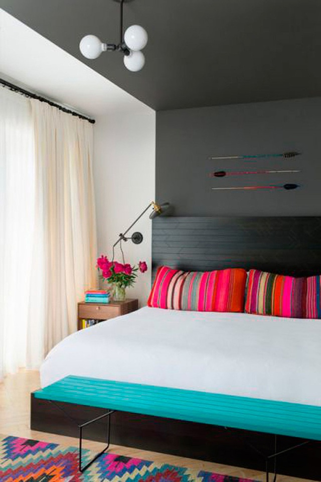 Những chiếc gối màu sắc rực rỡ và chiếc ghế băng màu xanh dương nổi bật trong không gian phòng ngủ chủ yếu là sắc màu trung tính.