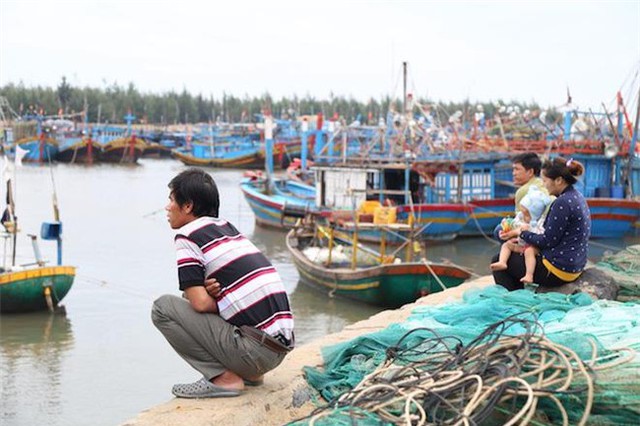 Trong khi c&aacute;c ngư d&acirc;n đang gia cố t&agrave;u thuyền ở dưới nước th&igrave; người nh&agrave;, lối x&oacute;m ngồi tr&ecirc;n bờ theo d&otilde;i.