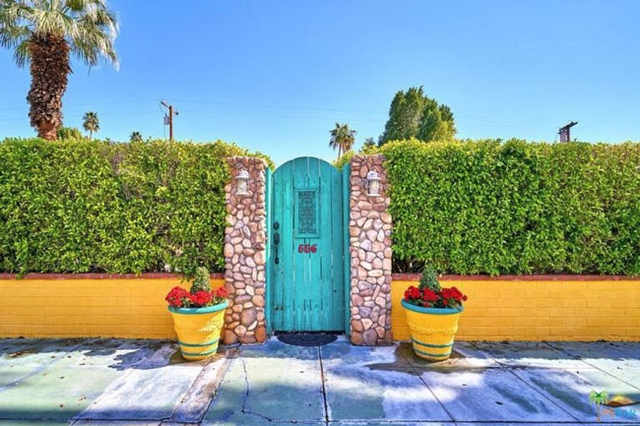 Ngôi nhà gây chú ý ngay từ hàng rào bằng cây xanh được cắt tỉa gọn gàng, bờ tường gạch sơn vàng rực và cánh cổng nhỏ màu xanh bắt mắt.