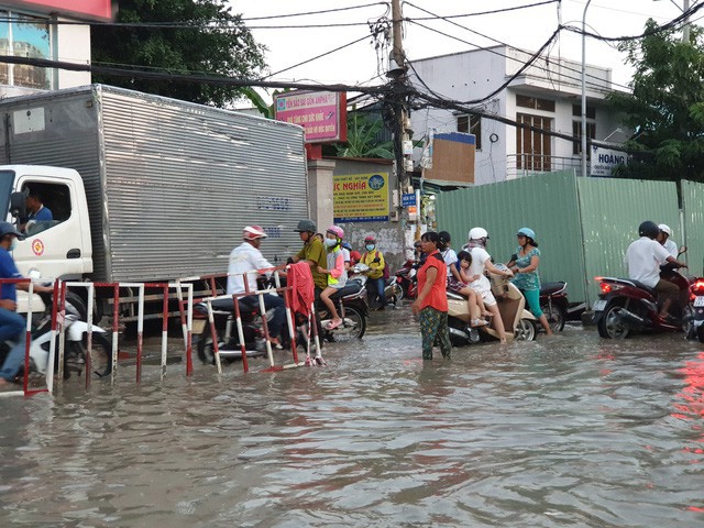 Trong ảnh l&agrave; chị Nga (l&agrave;m nghề b&aacute;n b&aacute;nh lọt) khi đi b&aacute;n ngang qua đ&acirc;y thấy cảnh ngập nước, kẹt xe n&ecirc;n bỏ cả xe b&aacute;nh chạy ra điều tiết giao th&ocirc;ng, đẩy xe gi&uacute;p d&acirc;n
